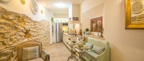 A cozy interior with a stone wall, a sofa, a table, and a kitchen in the background.