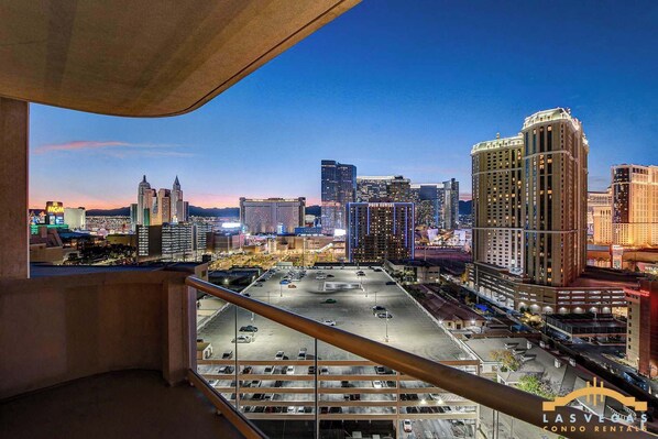 A cityscape view from a balcony overlooking a parking area with multiple buildings and a clear sky.