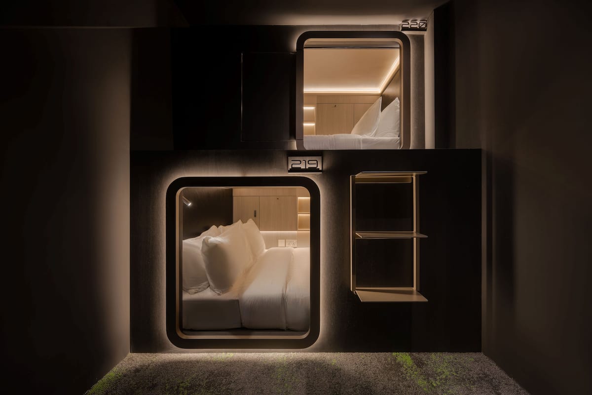 Una habitación compacta y moderna con cama, una mesita de noche pequeña y estantería empotrada.