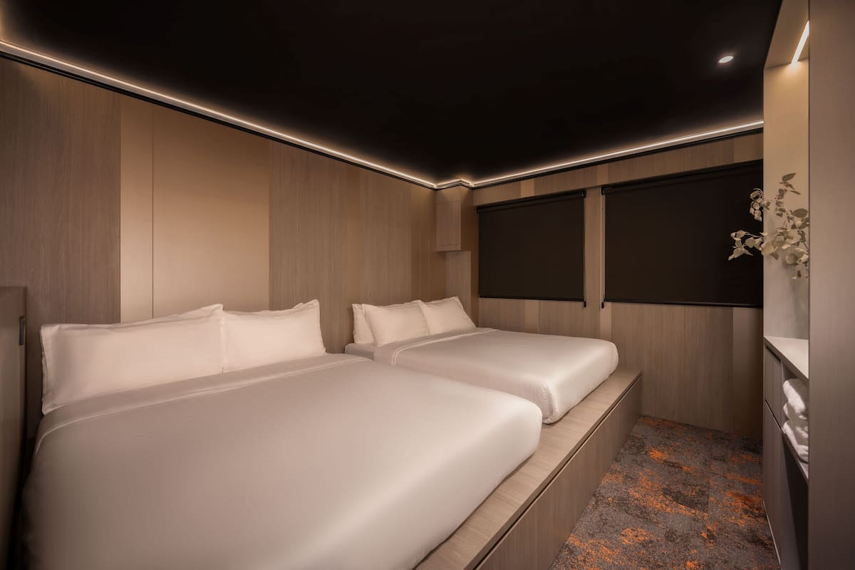 Una habitación de hotel moderna con dos camas, un ventanal grande y una pequeña zona de escritorio.