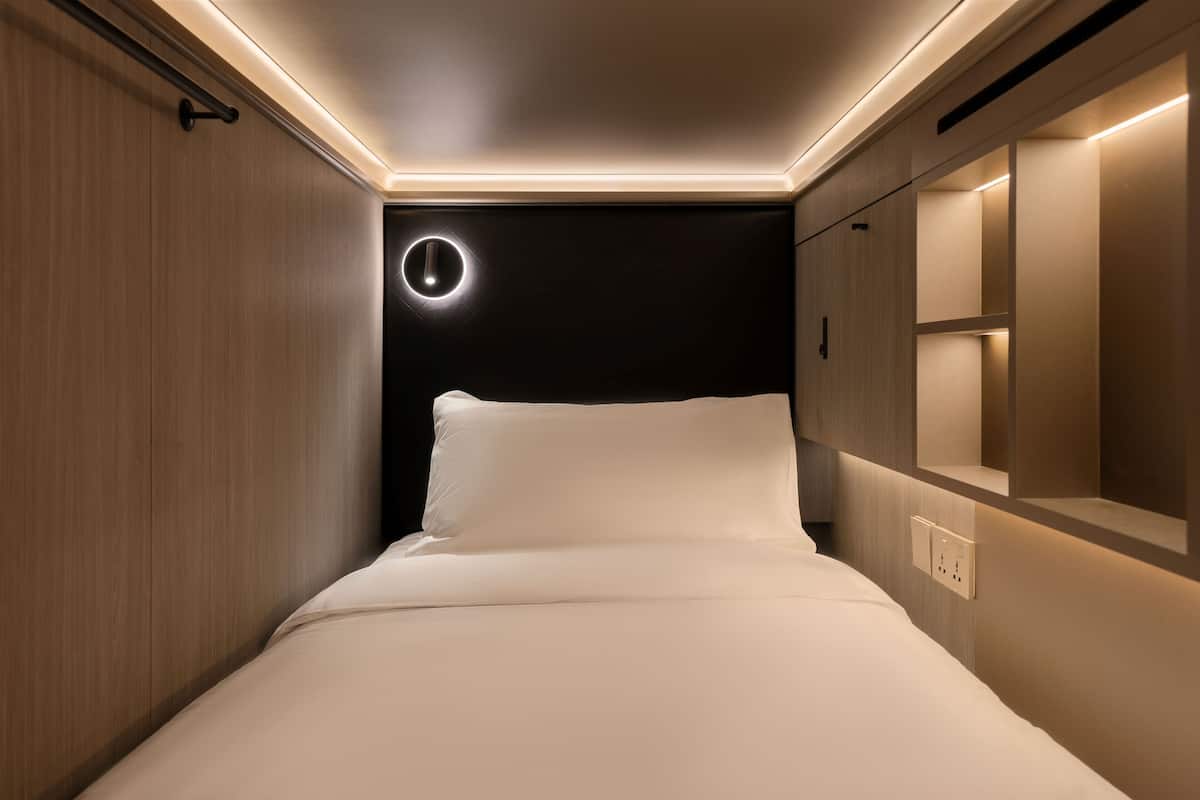 Un dormitorio moderno y funcional, con una lámpara circular sobre la cama, un armario empotrado y una mesita de noche.