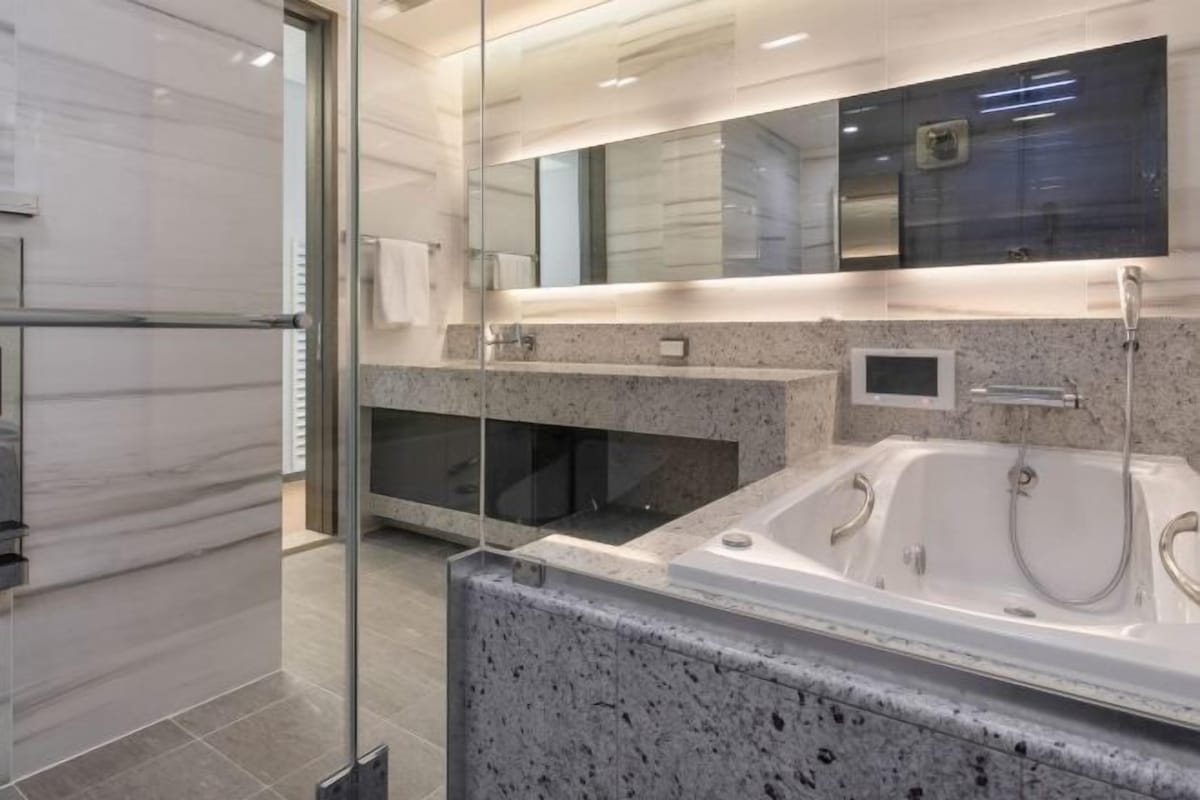 A modern bathroom with a glass shower enclosure, a large bathtub, and a vanity with a mirror.