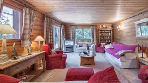 Interior acogedor de una cabaña de troncos con techo de madera, chimenea, sofá, mesa de centro y estantería.