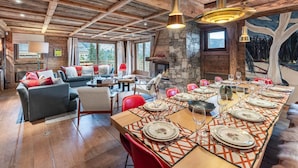 Un interior rústico con una larga mesa de comedor dispuesta para una comida, un rincón de estar acogedor con chimenea y una pared de piedra.