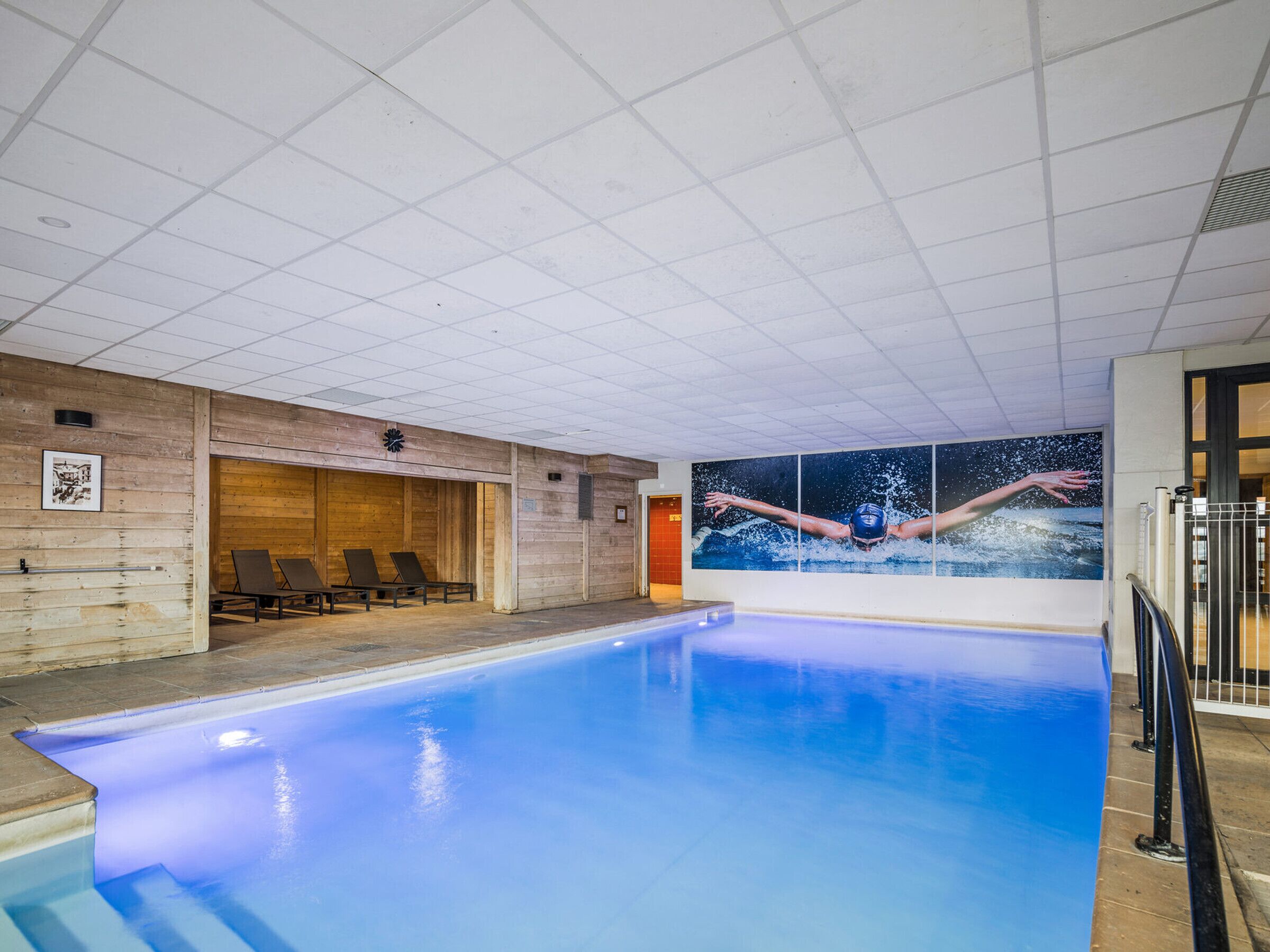 An indoor swimming pool with a blue water feature, wooden walls, and a large mural of a swimmer.