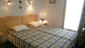 Ein Doppelbett mit karierter Bettdecke, zwei Kissen, einem Holz-Kopfteil, einer Nachttischlampe und einer Wandleuchte.