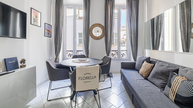 Una sala de estar moderna con un sofá gris, una mesa redonda de comedor con sillas y un televisor montado en la pared.