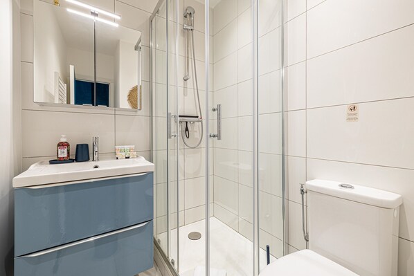 Un baño moderno con ducha de vidrio, azulejos blancos, un lavamanos con gabinete azul y un inodoro.