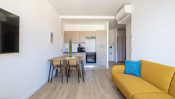 A modern living room with a sofa, a dining table with chairs, and a kitchen in the background.