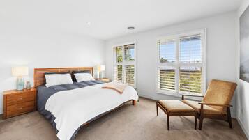 A bedroom with a bed, bedside tables, a chair, and large windows.
