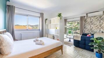 A modern hotel room with a bed, a sofa, a small table, and a view of the outdoors.