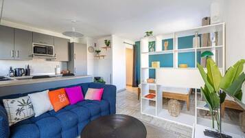 A modern living room with a blue sofa, a coffee table, and a white shelving unit with decorative items.