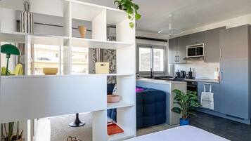 A modern kitchen with grey cabinets, a microwave, and a coffee maker. There is a blue sofa and a plant in the living area.