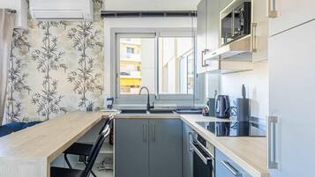 A compact kitchen with a window, a microwave, a kettle, and a sink.