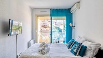 A bedroom with a bed, a TV mounted on the wall, and a window with a view of buildings outside.