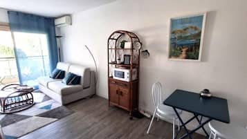 A living room with a sofa, a coffee table, a dining table, a chair, a bookshelf, and a painting on the wall.