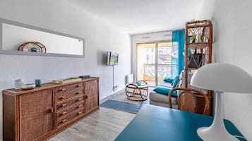 A modern living room with a blue table, wicker furniture, a TV, and a view of the outside.