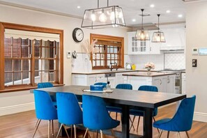 Une cuisine moderne avec des meubles blancs, un îlot central en bois et des chaises bleues disposées autour d’une table centrale.