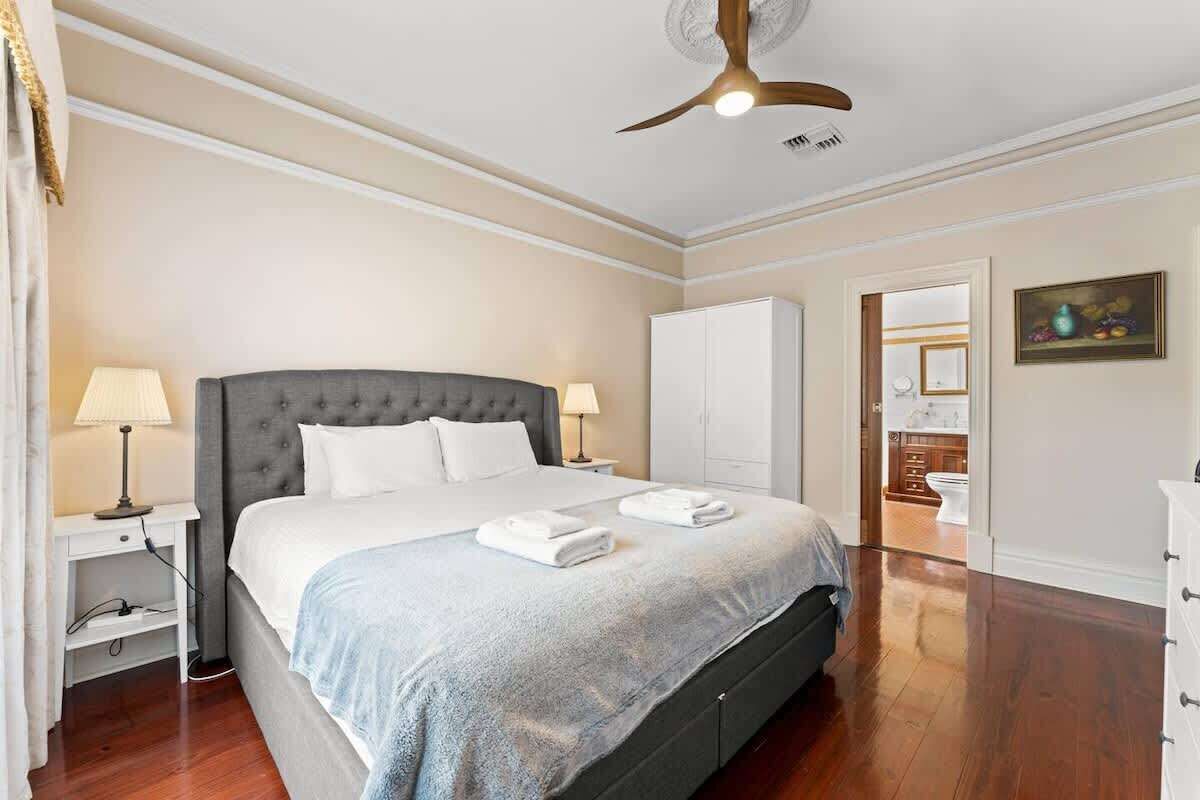 A neatly arranged bedroom with a large bed, bedside lamps, a wardrobe, and a ceiling fan.
