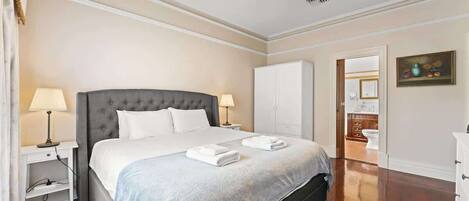 A neatly arranged bedroom with a large bed, bedside lamps, a wardrobe, and a ceiling fan.