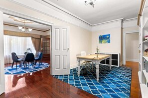 A dining area with a round table and chairs, a blue patterned rug, and a bookshelf in the background.