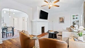 A modern living room with a fireplace, a ceiling fan, and a dining area with a table and chairs. - Classic Meets Contemporary I Minutes to Cle Clinic (Cleveland Heights)