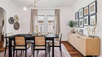 Comedor con mesa negra, cuatro sillas, un tapete estampado y un mueble de madera con marcos de cuadros.