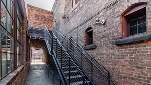 A narrow alleyway with a metal staircase leading up to a building with brick walls and large windows.
