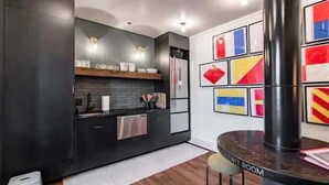 A modern kitchen with dark cabinetry, stainless steel appliances, and a white countertop. There is a small stool and a table with a label that reads "LEWIT ROOM".