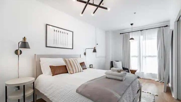 A modern bedroom with a large bed, bedside tables, a framed picture, and a window with curtains.