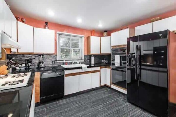 Una cocina moderna con electrodomésticos negros, armarios blancos y una ventana sobre el fregadero.