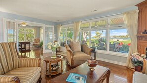 A spacious living room with a large window, a wooden coffee table, a striped armchair, and a beige sofa.