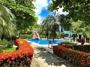 A landscaped pool area with a waterfall feature, surrounded by well-maintained hedges and palm trees. - Casa Verde 2b/2b Completely Renovated Ground Unit (Playas Del Coco)