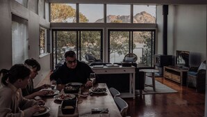 A dining area with a large table, chairs, and a view of a lake and mountains through large windows. - Sentinel at Freycinet (Glamorgan-Spring Bay)