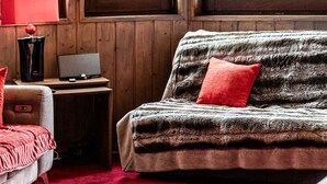 A cozy room with a wooden interior, a sofa with a red cushion, a red lamp, and a laptop on a small table. - Le Belvédère - IMMODREAMS - Avoriaz (Avoriaz)