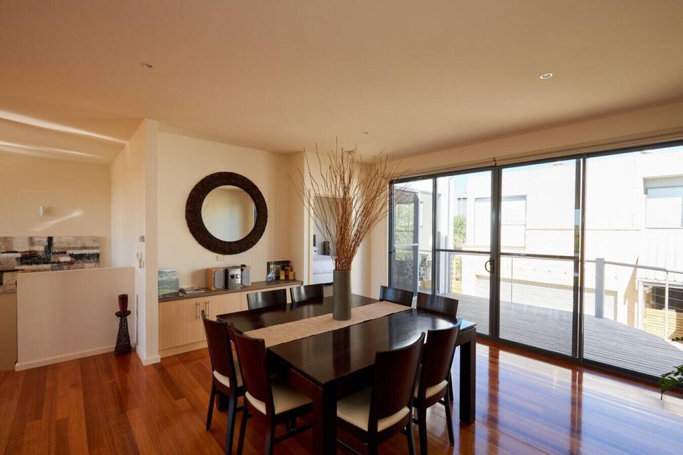 A modern dining area with a large table, chairs, and a view of the outdoors through large windows.