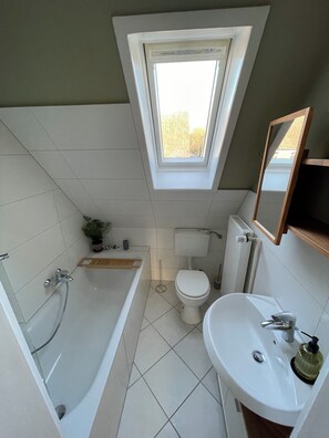 Un bagno compatto con finestra a lucernario, una vasca, un water e un lavabo.
