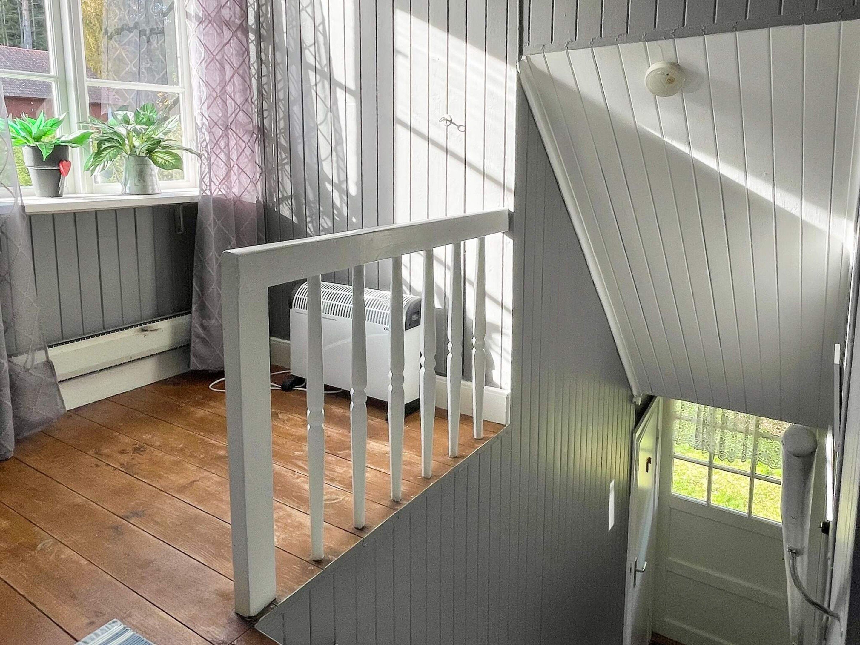 Una habitación con piso de madera, barandal blanco y una ventana con cortinas.