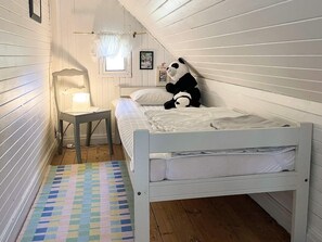 A single-bed room with a wooden floor, a bedside table with a lamp, a colorful rug, and a panda plush toy on the bed. - 7 Person Holiday Home in Horn (Horn)
