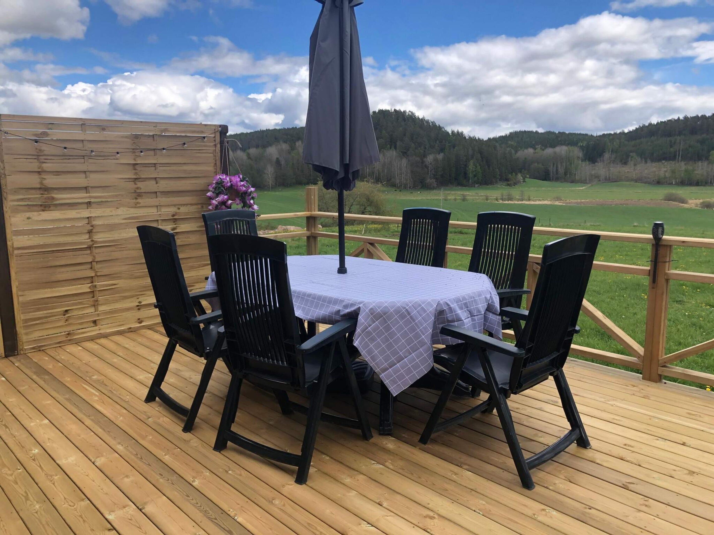 A deck with a table and chairs, a wooden fence, and a view of a green landscape.