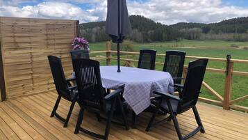 A deck with a table and chairs, a wooden fence, and a view of a green landscape.