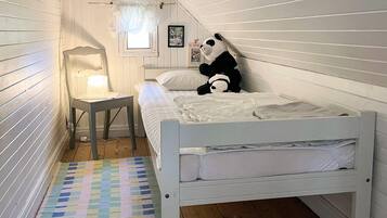 A white wooden room with a bed, a small table with a lamp, a colorful rug, and a panda plush toy on the bed.