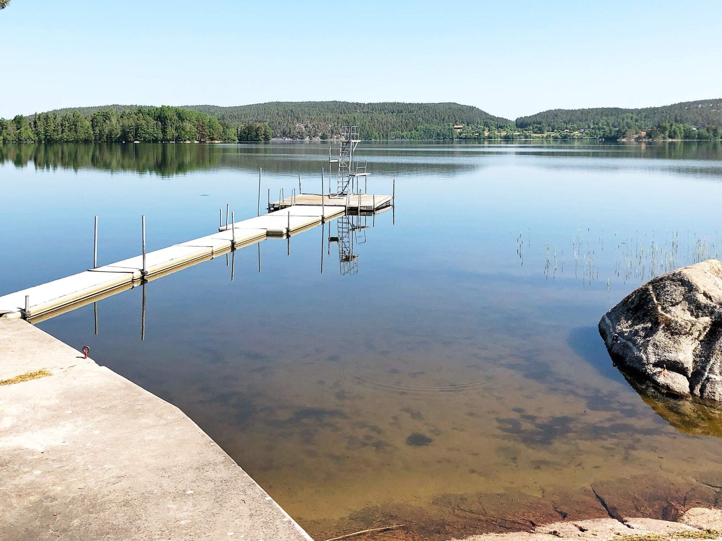 Un lac paisible, avec une jetée en béton qui s’avance dans l’eau, entouré de collines boisées.