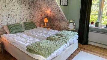 A bedroom with a bed, pillows, a bedside lamp, a window with a view, and a radiator.