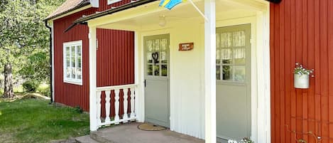 A red wooden house with a white porch, a flag, and potted plants.
