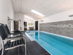A swimming pool with black lounge chairs, a tiled floor, and a wall with a mosaic pattern. - 8 Person Holiday Home in Rodby (Rodby)