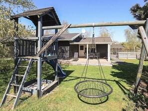 A wooden play structure with a slide and a swing set. - 8 Person Holiday Home in Rodby (Rodby)
