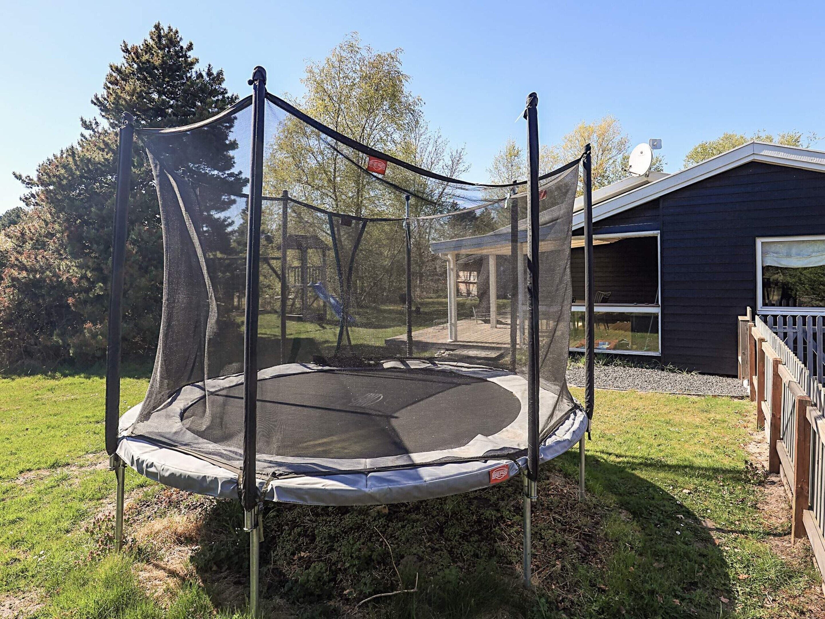 A trampoline with a safety net, set up in a grassy yard with a house in the background.