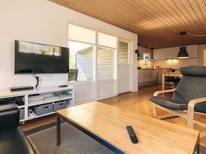 A living room with a flat-screen TV, a wooden coffee table, a grey armchair, and a sofa. - 8 Person Holiday Home in Rodby (Rodby)