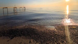 Une plage avec un ciel dégagé et le soleil se couchant sur l’eau.
